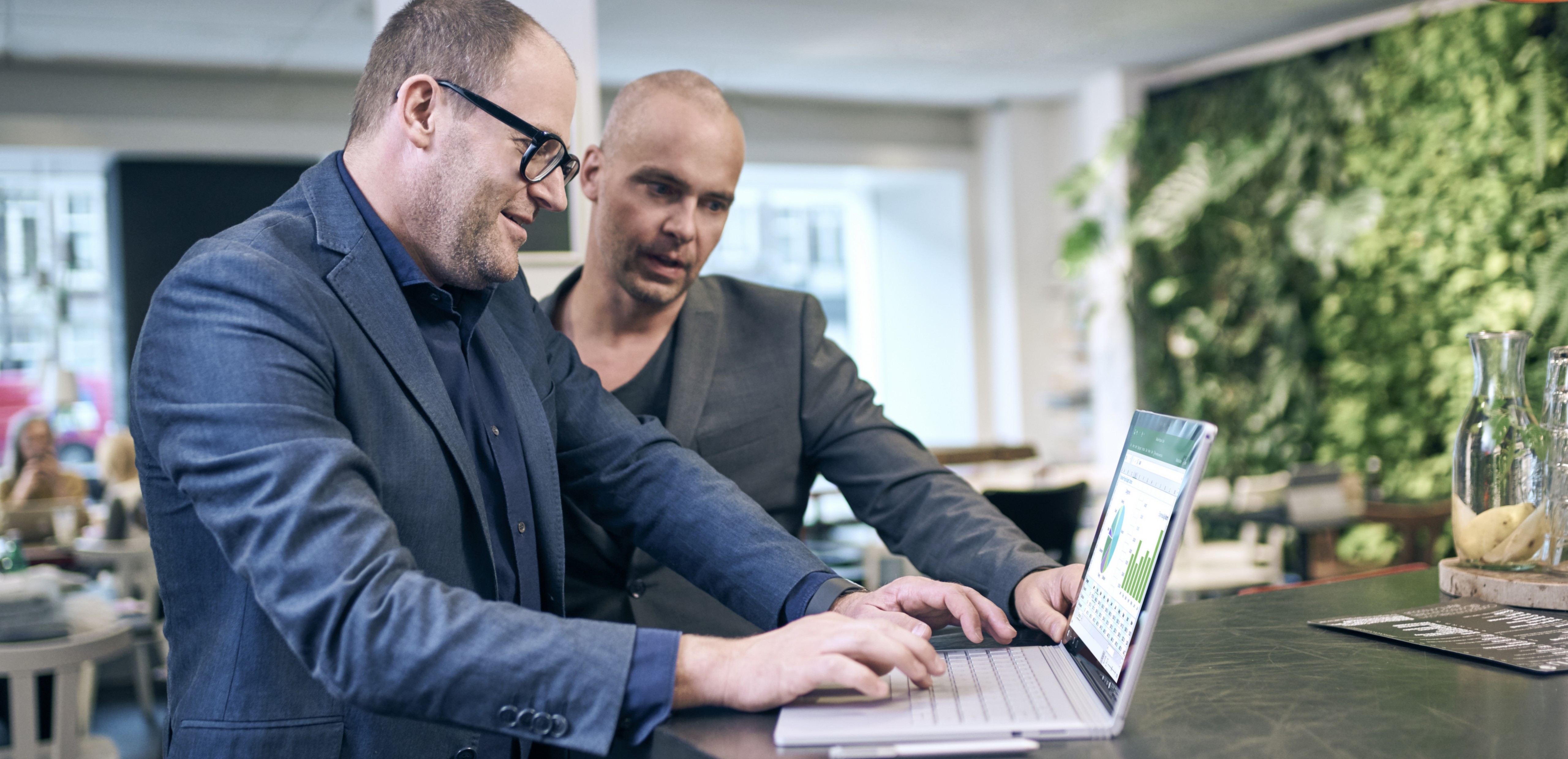 Two men in an office standing at a desk working on a Surface Book.