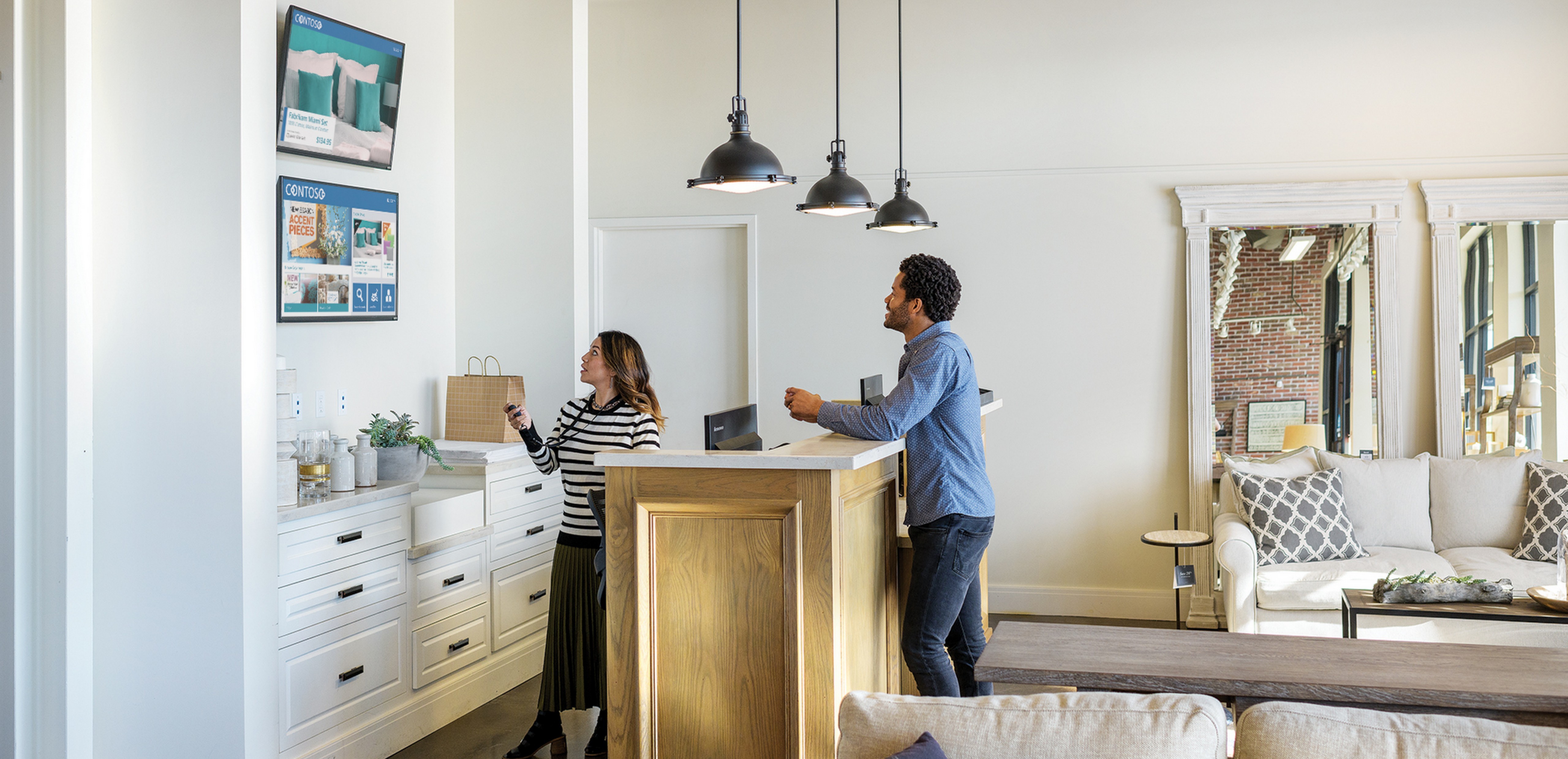 Man and woman in a room looking at two tv screens.