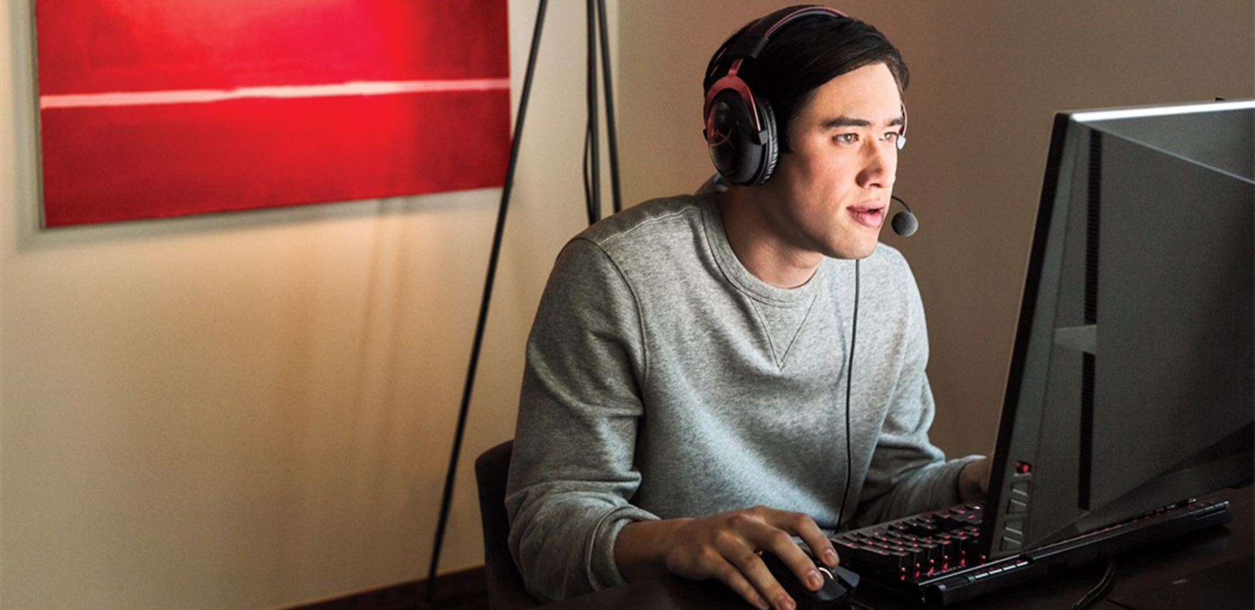 Man sitting in front of computer monitor with headphones, tapping a mouse