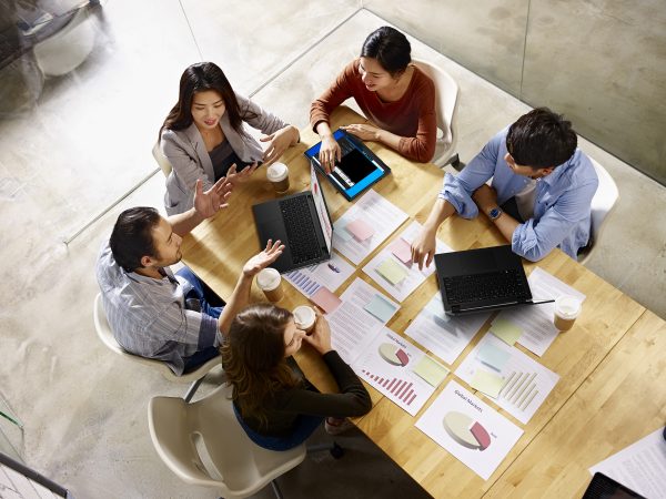 Group of 5 sitting at a table working with paper charts and Acer laptops, seen from above